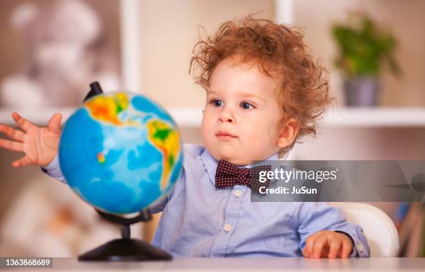 kindheit, kinder erholung und unterhaltung konzept. schöne lockige baby junge mit der weltkugel auf dem tisch zu hause. vorschul-kleinkind-studium in der heimschule. kinderbildung, selbstisolation, coronavirus ausbruch soziale trennung oder homeschooling. - baby sun hat stock-fotos und bilder