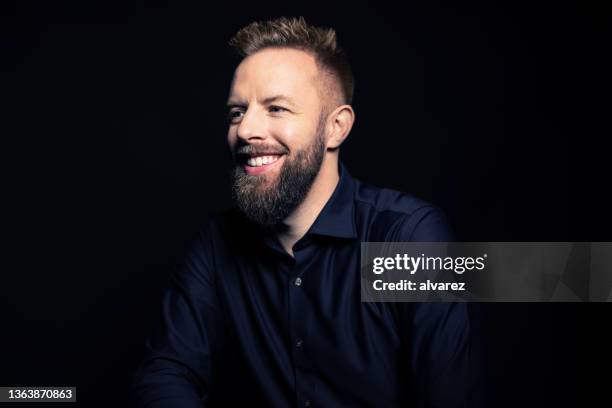 happy young man with beard looking away and smiling - black background portrait stockfoto's en -beelden