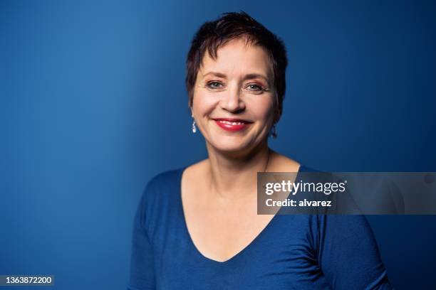 portrait of smiling mature woman with short hair on blue background - blue background portrait bildbanksfoton och bilder