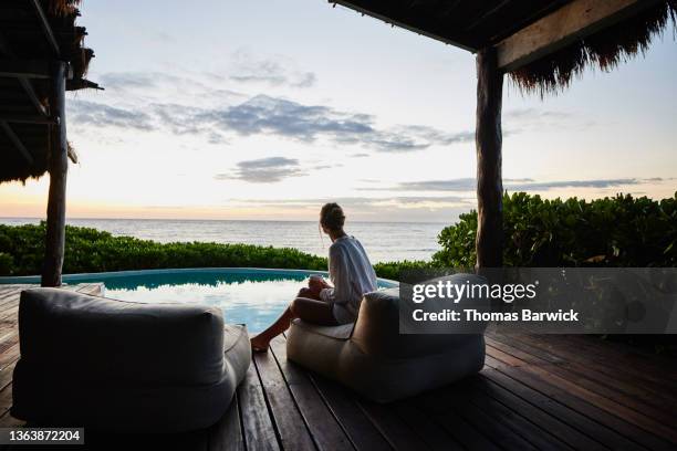 wide shot rear view of woman enjoying sunrise next to pool at luxury suite at tropical resort - resort enjoy ストックフォトと画像