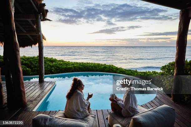 wide shot of female friends in discussion while sitting poolside at luxury suite of tropical resort at sunrise - connect friends sunrise photos et images de collection