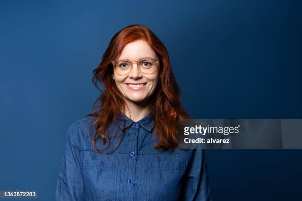 青いスタジオの背景に赤い髪を持つ笑顔の成熟した女性の肖像画 - one mature woman only ストックフォトと画像