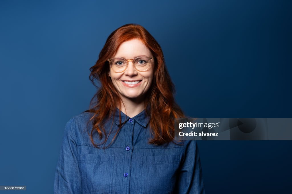 Retrato de uma mulher madura sorridente com cabelos vermelhos no fundo do estúdio azul
