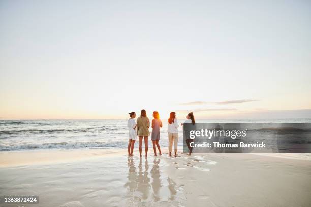 wide shot of female friends hanging out on tropical beach watching sunrise - cinco personas fotografías e imágenes de stock