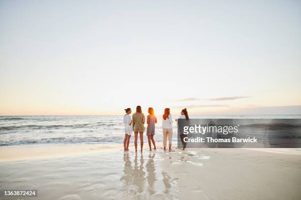 wide shot of female friends hanging out on tropical beach watching sunrise - five people stock pictures, royalty-free photos & images