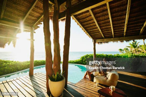wide shot of female friends relaxing on pool deck of luxury tropical vacation rental at sunrise - sun deck stock pictures, royalty-free photos & images