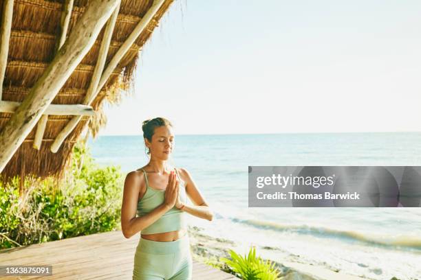 medium wide shot of woman practicing yoga in ocean front pavilion at tropical resort - pavilion stock pictures, royalty-free photos & images