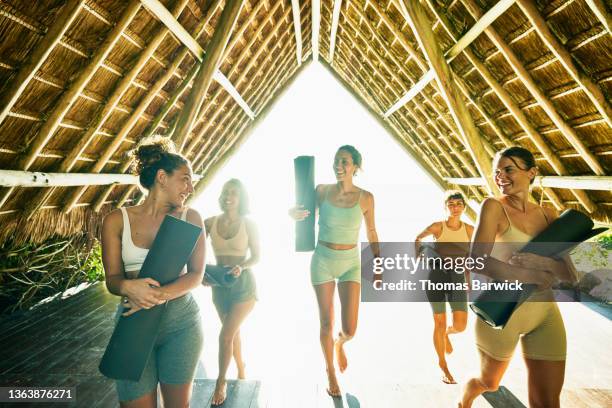 wide shot of smiling female friends finishing yoga class in ocean front pavilion at tropical resort - self improvement stockfoto's en -beelden