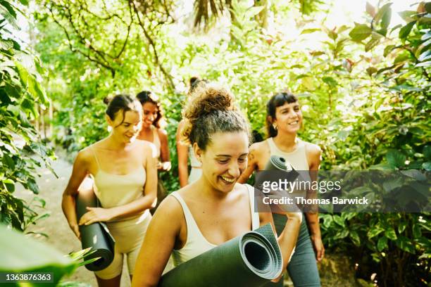 Medium wide shot of smiling female friends walking through path in jungle after taking yoga class at tropical resort