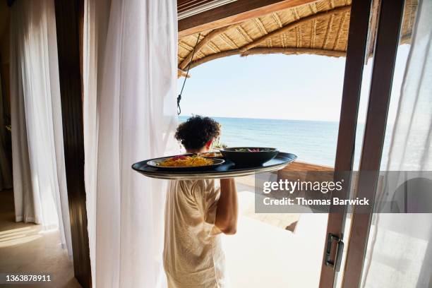 medium wide shot of waiter bringing breakfast to guests on deck of luxury suite at tropical resort - holiday arrival stock pictures, royalty-free photos & images