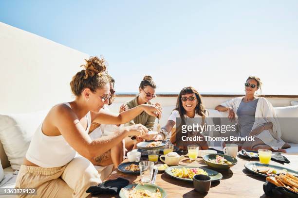 medium wide shot of smiling female friends sharing breakfast on deck of luxury suite at tropical resort - friendship stock pictures, royalty-free photos & images