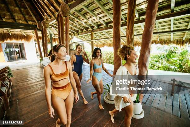 wide shot of smiling and laughing female friends walking through outdoor pavilion of luxury suite at tropical resort - swimwear stock-fotos und bilder