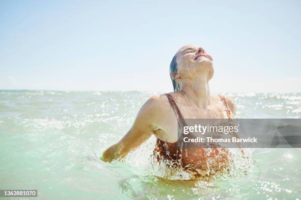 medium wide shot of smiling woman emerging from ocean - emergence stock-fotos und bilder