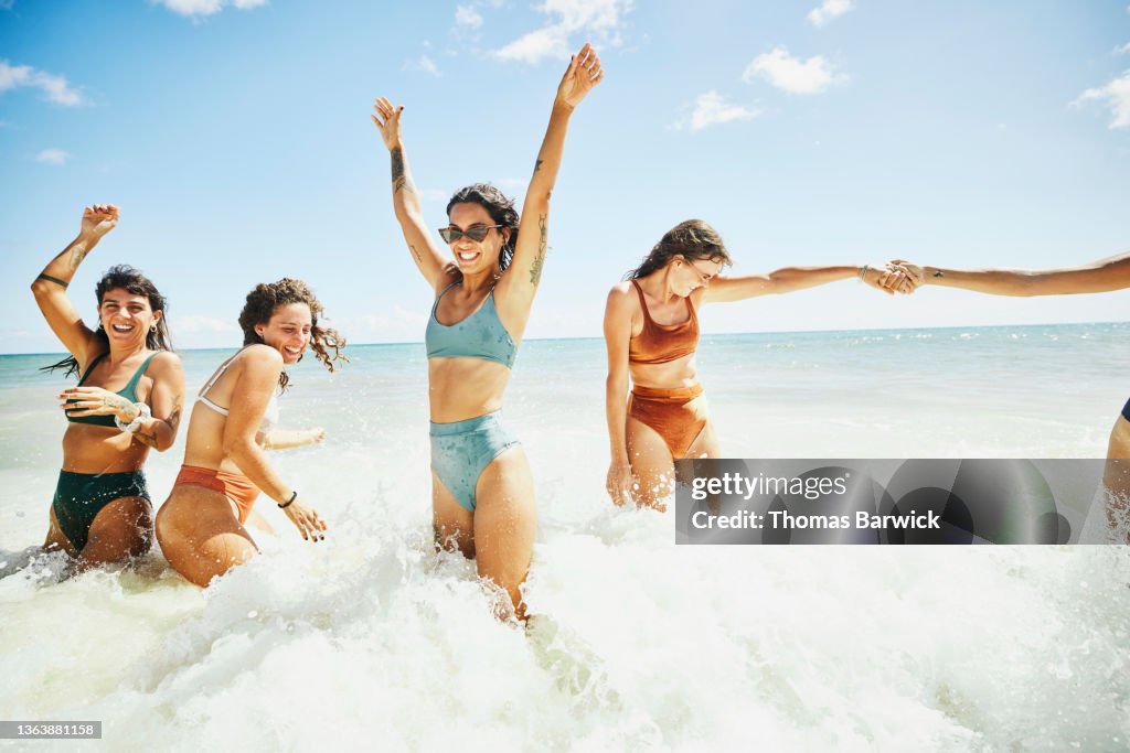 Wide shot of laughing and smiling female friends playing in surf at tropical beach