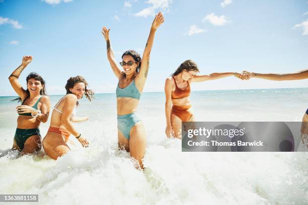 wide shot of laughing and smiling female friends playing in surf at tropical beach - badkläder bildbanksfoton och bilder