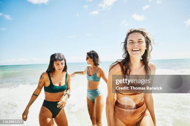 medium wide shot of laughing and smiling female friends playing in surf at tropical beach - swimsuit stockfoto's en -beelden