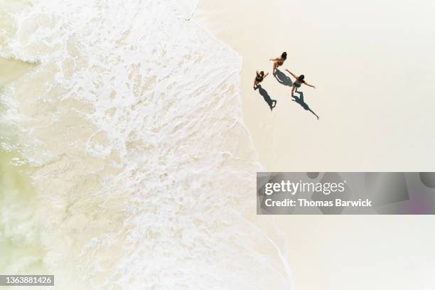 extreme wide shot overhead view of female friends walking on tropical beach - female golf stockfoto's en -beelden