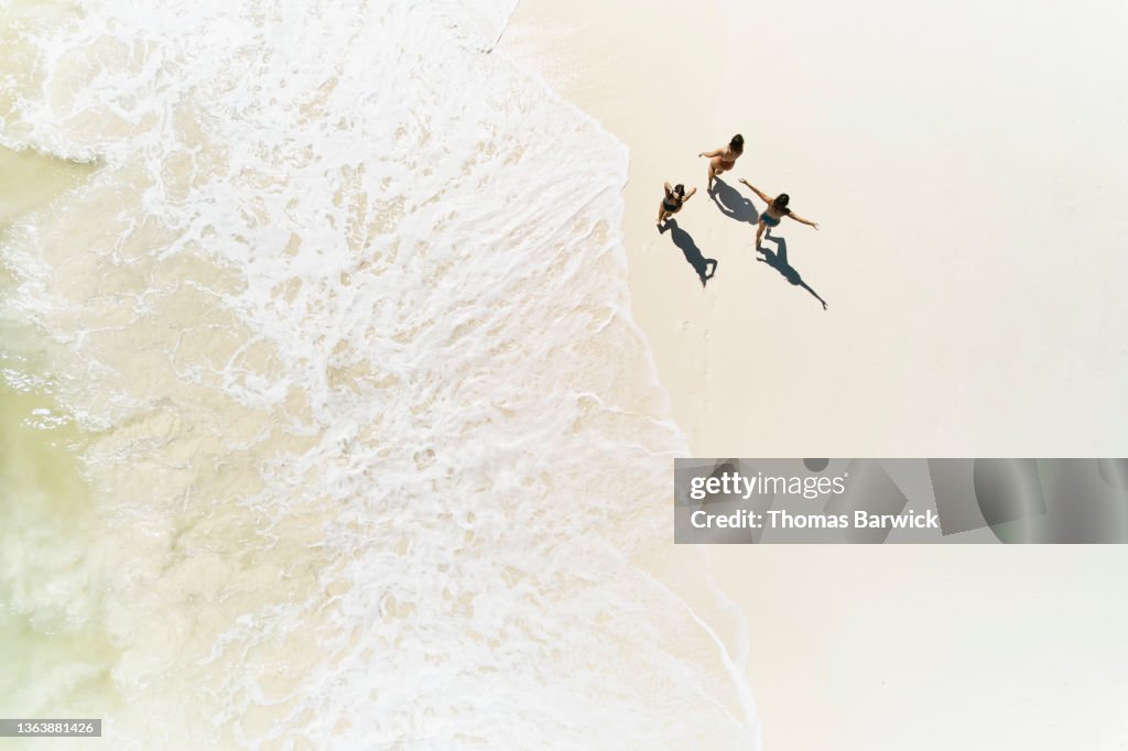 Extreme wide shot overhead view of female friends walking on tropical beach