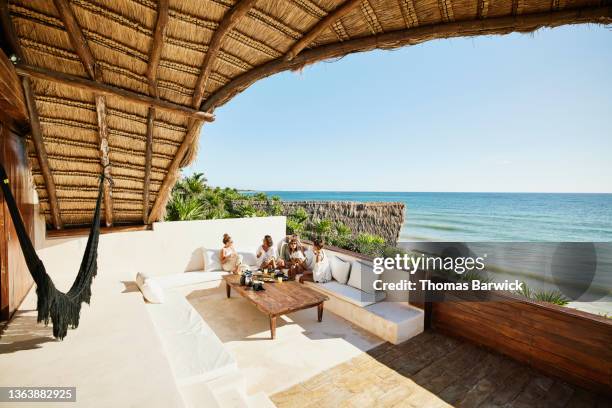 extreme wide shot of female friends enjoying breakfast on deck of luxury suite overlooking ocean at tropical resort - dining overlooking water stock-fotos und bilder
