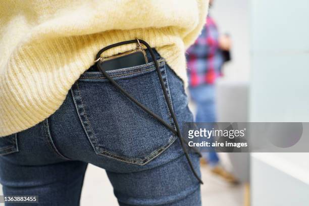 close-up of midsection of a young woman wearing casual clothing with a smartphone in her jeans pocket at her workplace against an unrecognizable person standing in the background - jeans poche photos et images de collection