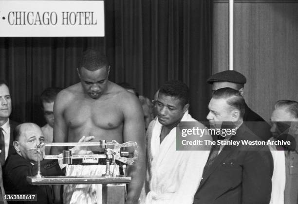 Photo shows Sonny Liston weighing-in and Floyd Patterson observing Liston's weight at the Sheraton Hotel in Chicago before their Heavyweight Title...