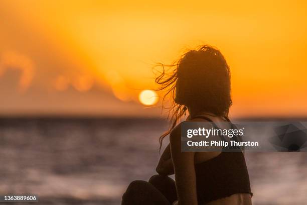 woman sitting at edge of ocean watching golden sunset - watching sunset stock pictures, royalty-free photos & images