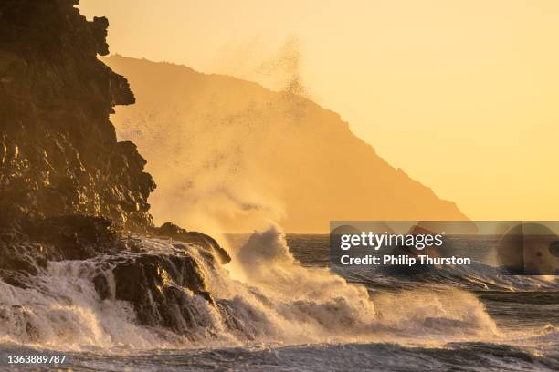 waves crashing against rocky coastline during a golden sunset - rocky coastline stock pictures, royalty-free photos & images