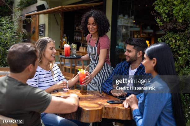 glückliche kellnerin, die einer gruppe von freunden in einem restaurant getränke serviert - kellner oder kellnerin stock-fotos und bilder