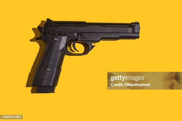 black gun with direct light and hard shadow on yellow background. murder, violence, gun, shooting, police, bodyguard, hitman and army concept. - arme à feu photos et images de collection