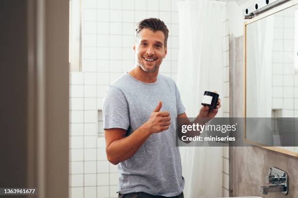 hombre blanco sosteniendo un frasco de crema facial en el baño - hombre crema facial fotografías e imágenes de stock