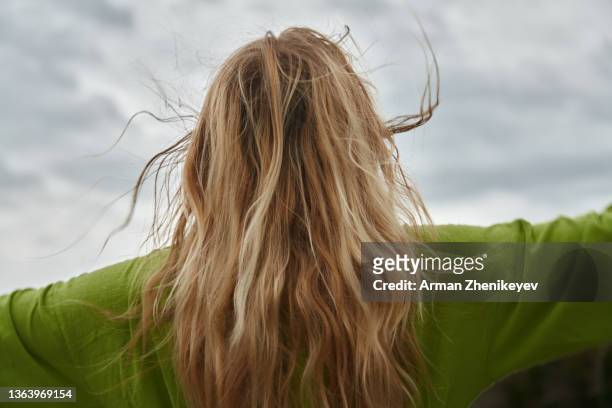 carefree blond woman wearing lime green dress looking up to the dramatic sky - hair flying stock-fotos und bilder