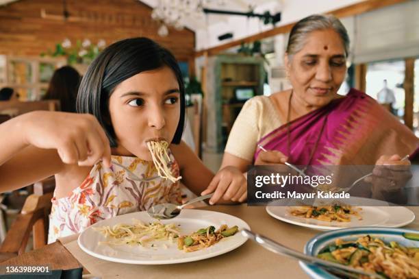 girl and grandmother eating noodles in a restaurant - indian restaurant stock pictures, royalty-free photos & images