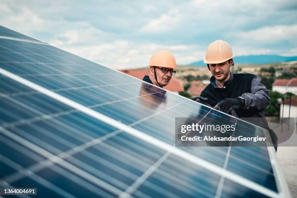 senior and junior workers on solar panel setup tightening stands on house roof - röra mot bildbanksfoton och bilder