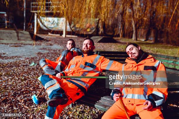three tired male street sweepers relaxing after work on playground bench - park service stock pictures, royalty-free photos & images
