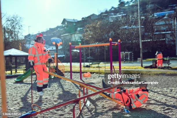 verrückte sanitärarbeiter, die nach der arbeit auf dem spielplatz mit wippen spielen - müllmann stock-fotos und bilder