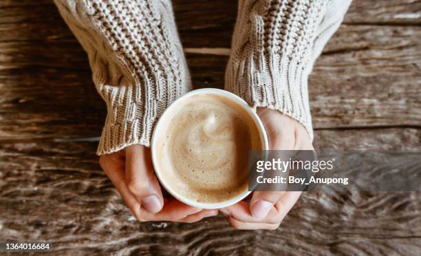 top view of woman hands holding a cup of hot milk coffee before drinking on wooden table. - taza de café fotografías e imágenes de stock