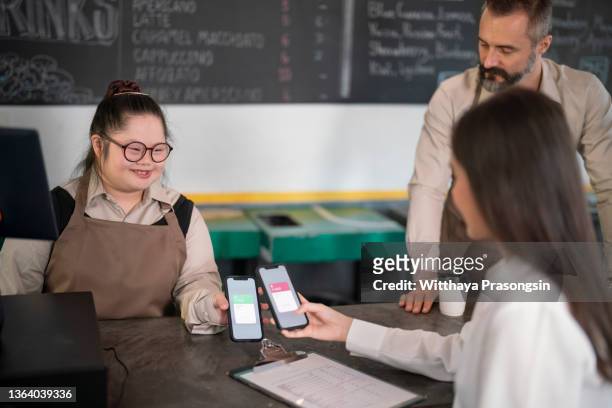 down syndrome, working in a coffee shop, sending and receiving mobile payments. - micro finance stock pictures, royalty-free photos & images