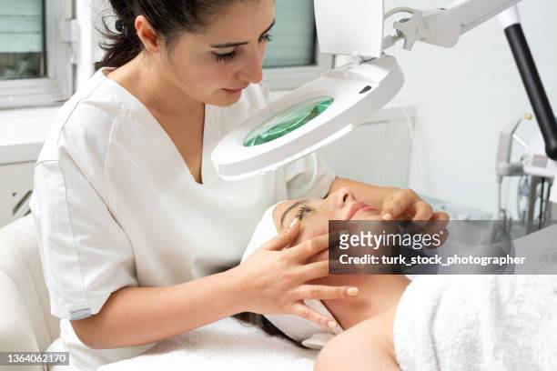 female cosmetologist doctor analyzing woman's skin analysing with magnifying glass - beautician stock pictures, royalty-free photos & images