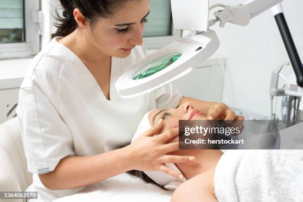 female cosmetologist doctor analyzing woman's skin analysing with magnifying glass - beauty treatment imagens e fotografias de stock