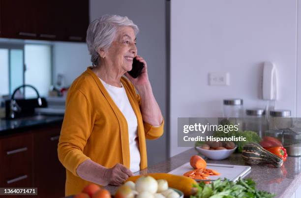 cheerful senior woman at home on a phone call while preparing a vegetarian meal - inside of pumpkin stock pictures, royalty-free photos & images