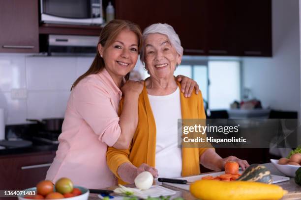 loving senior mom and daughter preparing a meal together facing camera with a toothy smile at home - mother daughter cooking stock pictures, royalty-free photos & images