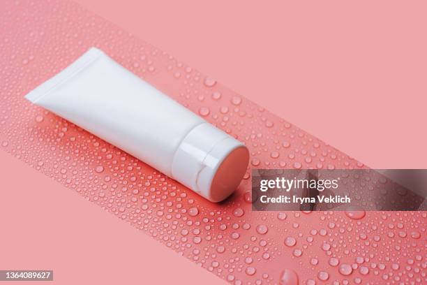 white tube with cosmetic face cream or hand cream, shower gel, shampoo on water drops on a pastel pink background. - 水滴　白 ストックフォトと画像