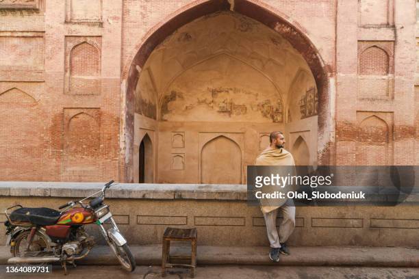 hombre sentado cerca de la mezquita en lahore - pakistan monument fotografías e imágenes de stock