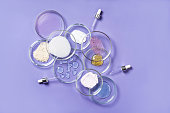 Cosmetic products, scrub, face serum and gel in many petri dishes on a pink background. Cosmetics laboratory research concept. Pastel violet background