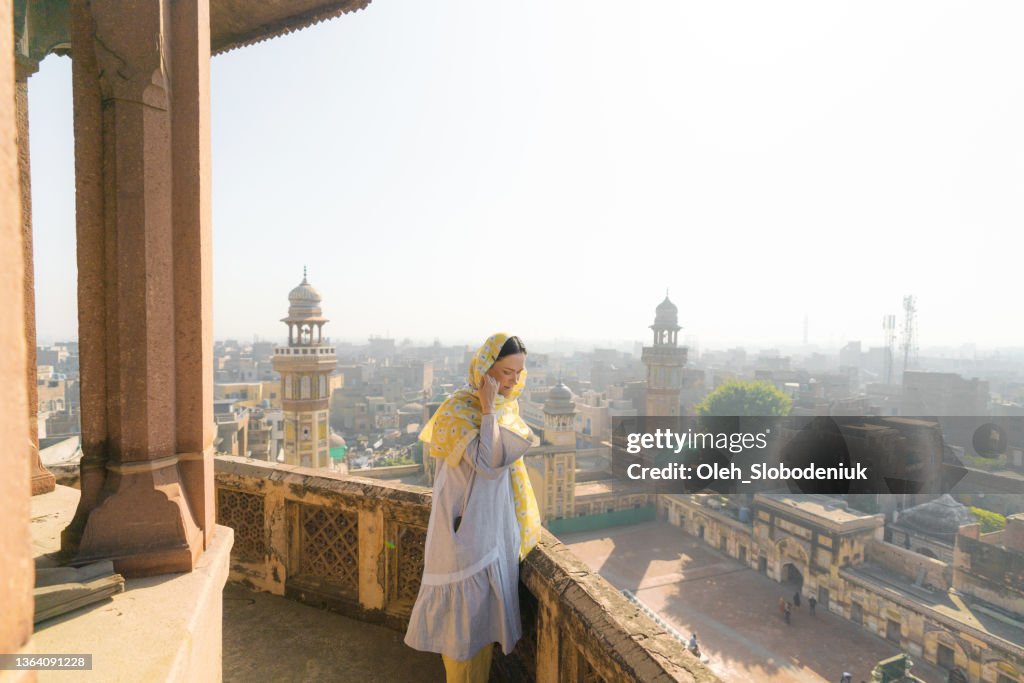Woman in hijab standing near the minaret and looking at Lahore city from above