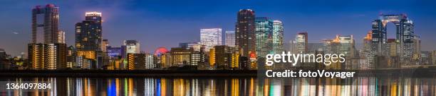 crowded cityscape of glittering skyscrapers reflecting night waterfront osaka japan - panoramic city stock pictures, royalty-free photos & images