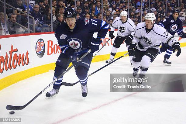Eric Fehr of the Winnipeg Jets carries the puck along the corner boards as Colin Fraser and Jack Johnson of the Los Angeles Kings give chase during...