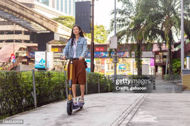 mujer montando motoneta en la acera de la ciudad - economía colaborativa fotografías e imágenes de stock