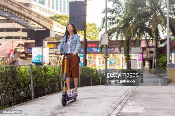 woman riding motor scooter on sidewalk of city - sharing economy stock pictures, royalty-free photos & images