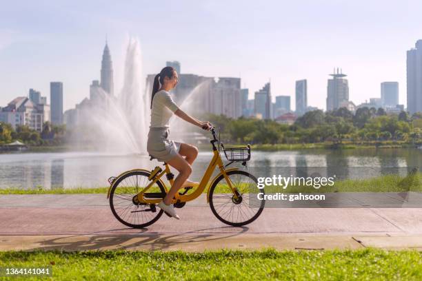 woman rented public bicycle, riding by lake in park - asian cycling stock pictures, royalty-free photos & images